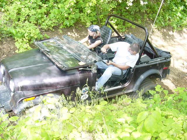 Jeep CJ-7 with windshield down, two people inside, driving through brush