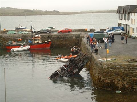 1989 Ford Bronco - A truck has tipped into the water at a harbor, with onlookers gathered on the dock.