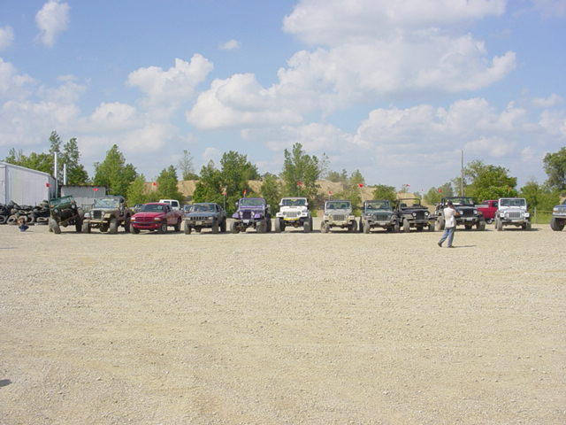 Several modified Jeeps and trucks parked in a lot with a person walking