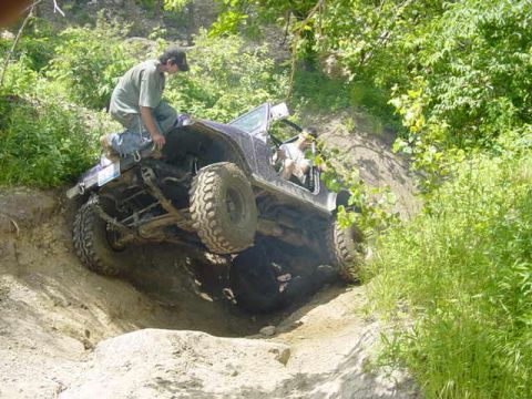 1992 Ford Bronco - A Jeep Wrangler navigates a steep, rocky incline with a driver perched on its hood.