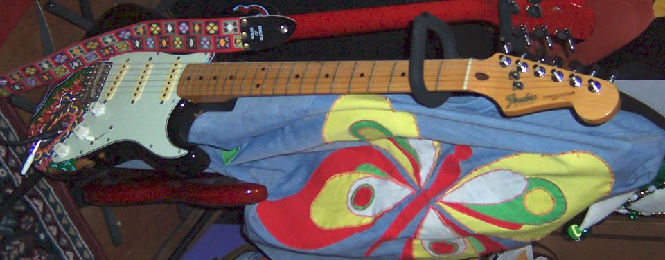 Fender electric guitar with patterned strap resting on blue butterfly-print fabric