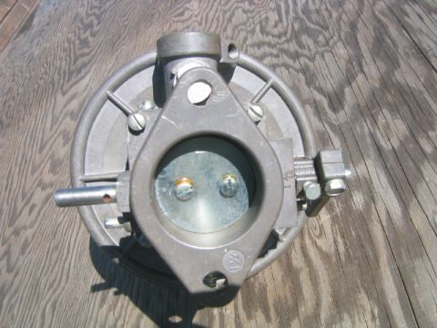1973 Ford F-100 - A carburetor part is shown against a wooden background, with visible screws and mounting hardware.