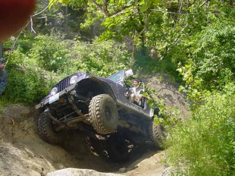 1992 Ford Bronco - A Jeep Wrangler navigates a challenging off-road trail, with one wheel significantly elevated.