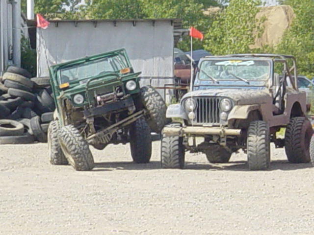 Two modified off-road vehicles parked on gravel, one green, one tan