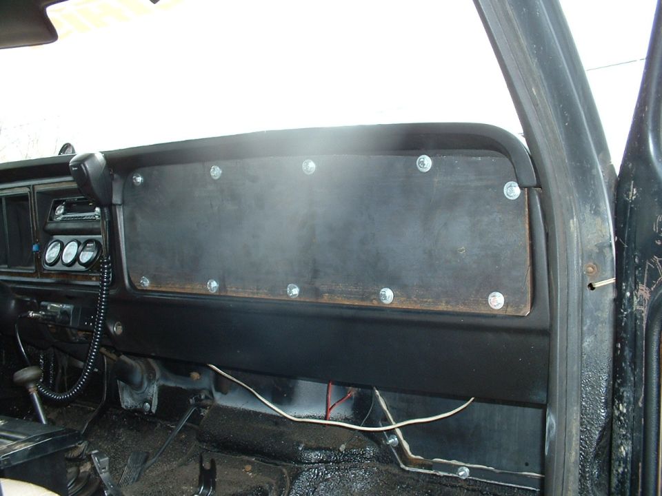 Dashboard of a vehicle with a custom wooden panel screwed over the center console. Gauges are visible to the left