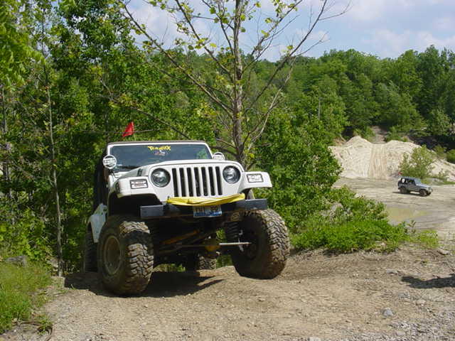 White lifted Jeep Wrangler TJ on large mud tires parked on a wooded trail