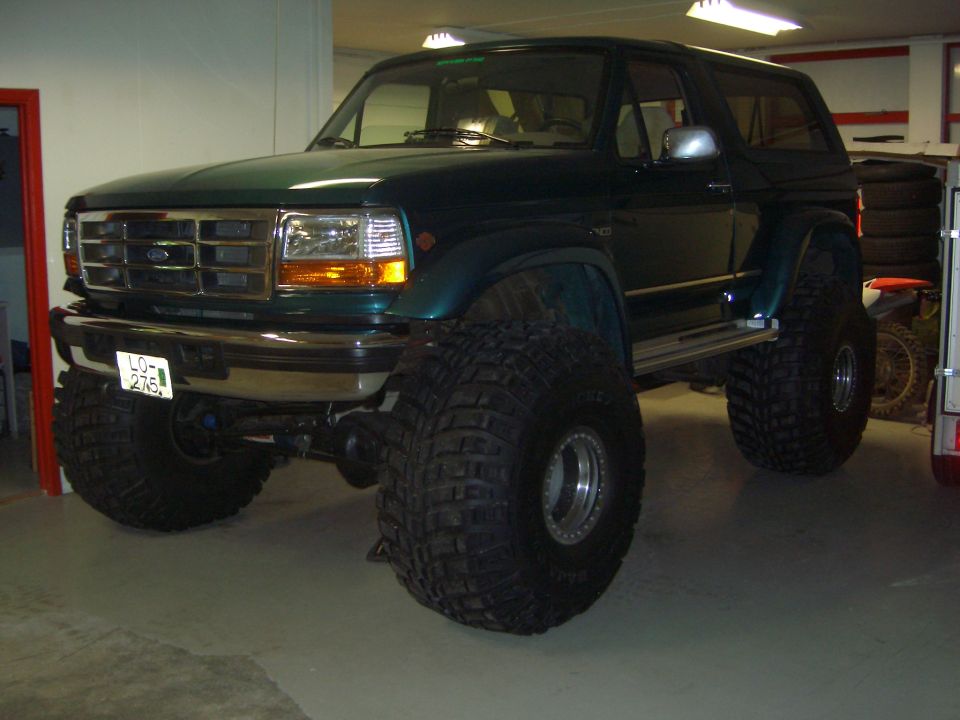 Dark green lifted Ford Bronco with huge tires on green LO-276 plate in garage
