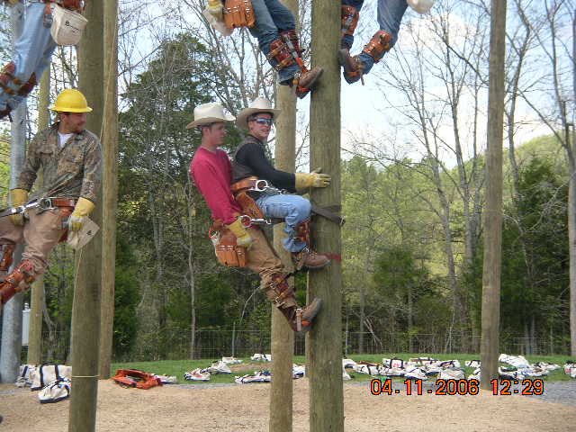 Linemen in safety gear climbing utility poles with ropes and harnesses