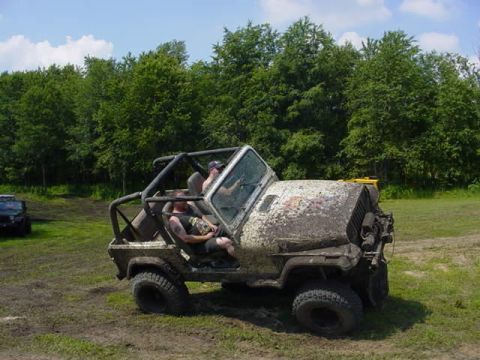 1992 Ford Bronco - Two people ride in a heavily mud-splattered off-road vehicle during an outdoor event.