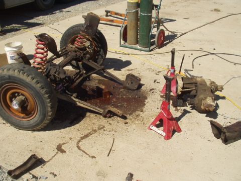 1993 Ford Bronco - Vehicle parts, including the front axle and transmission, are laid out on concrete with welding equipment nearby.
