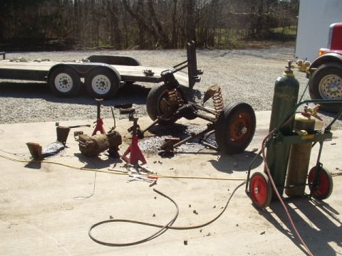 1993 Ford Bronco - Vehicle axle and transmission disassembled and supported by jack stands, with a trailer and welding equipment in the background.