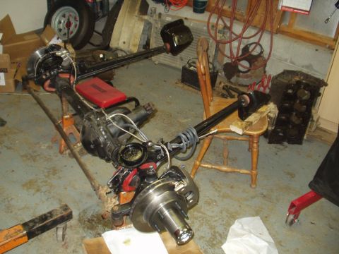 1993 Ford Bronco - A disassembled front axle assembly rests on jack stands in a garage, surrounded by tools and engine parts.