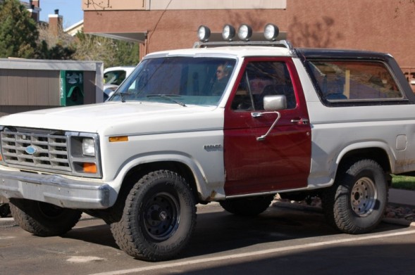 White and red two-tone full-size Ford Bronco with roof lights in a lot