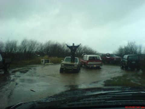1983 Ford Ranger - A person stands on a truck in a muddy field surrounded by other vehicles under a cloudy sky.