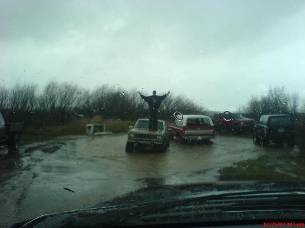 Person standing on a light-colored truck in a muddy area with several other trucks and SUVs visible