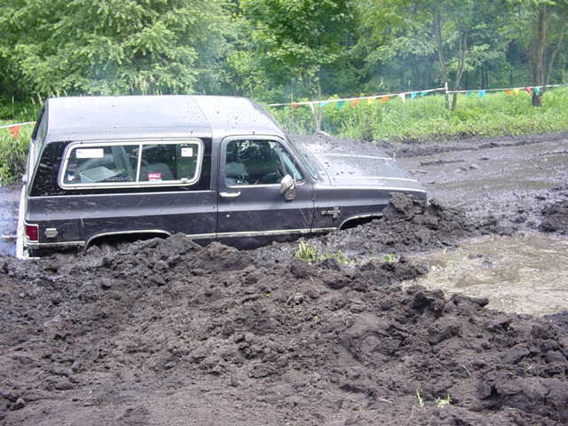 Square-body Chevrolet truck with camper shell stuck in deep mud
