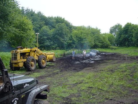 1992 Ford Bronco - A muddy off-road event features a front loader and a vehicle stuck in the mire.