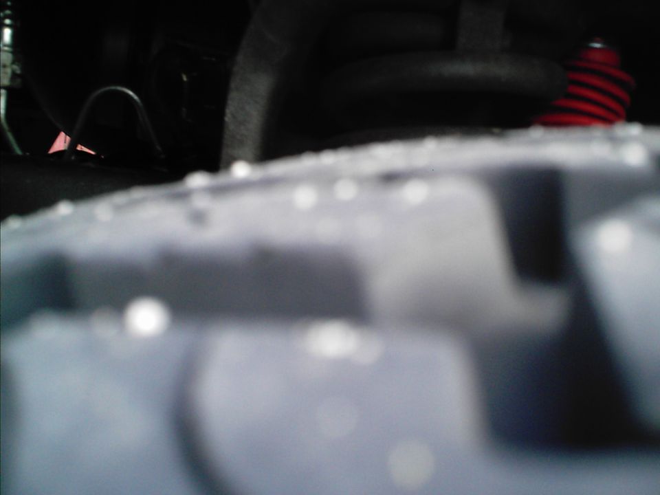 Close-up of a tire and suspension components, possibly from a truck or SUV. A red coil spring is visible
