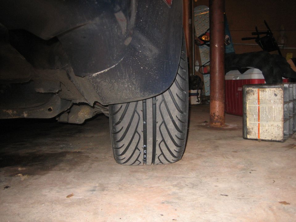 Close-up of a car's front tire and fender in a cluttered garage