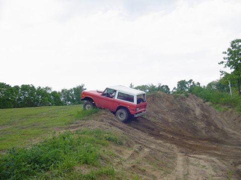 1992 Ford Bronco - A red Ford Bronco is shown navigating a steep dirt incline on a cloudy day.