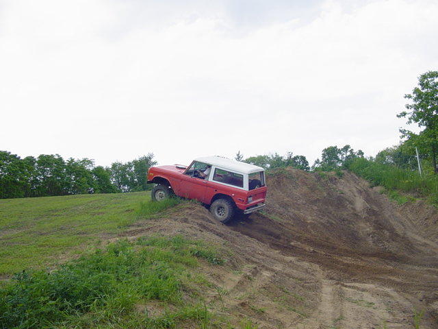 Red Ford Bronco climbing a dirt hill with trees in the background