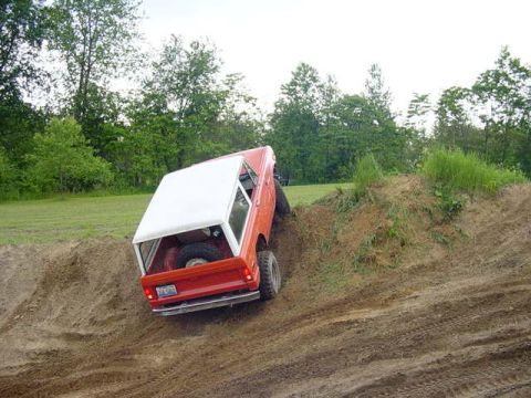 1992 Ford Bronco - A red SUV with a white top navigates a steep dirt incline, showing its rear profile.