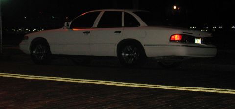 1997 Ford Crown Victoria - A white sedan is parked on the street at night, illuminated by streetlights and its own taillights.