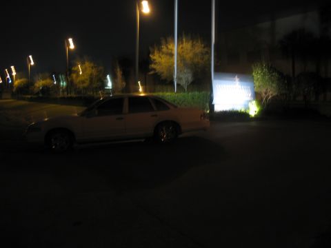 1997 Ford Crown Victoria - A light-colored sedan is parked outdoors at night, illuminated by streetlights.