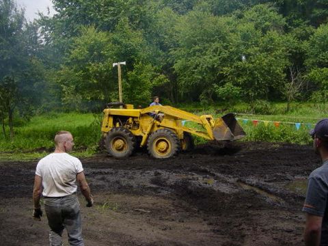 1992 Ford Bronco - A yellow front loader is seen working in a muddy field, with a person operating it and another person watching.