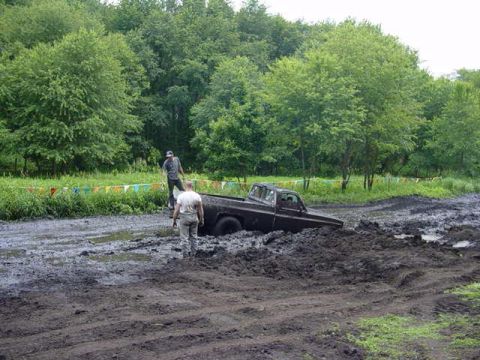 1992 Ford Bronco - Two people stand near a pickup truck that is deeply stuck in a muddy off-road course.