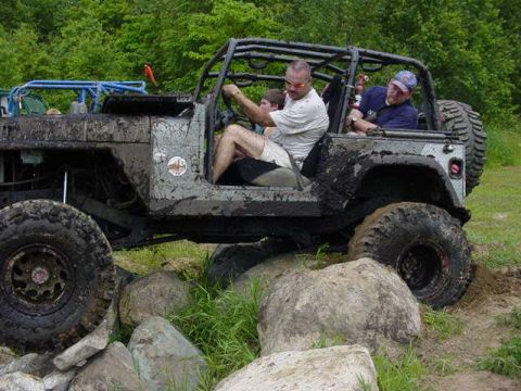 1992 Ford Bronco - An off-road vehicle, covered in mud, is driven over large rocks by its occupants.