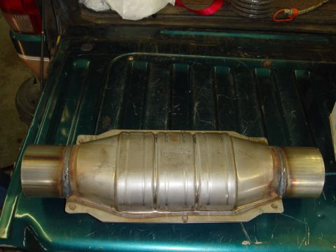 1996 Ford Bronco - A catalytic converter with visible text is placed on a dark green truck bed.