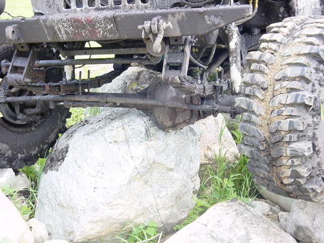 Mud-covered off-road vehicle front axle, suspension, and large tire resting on rocks