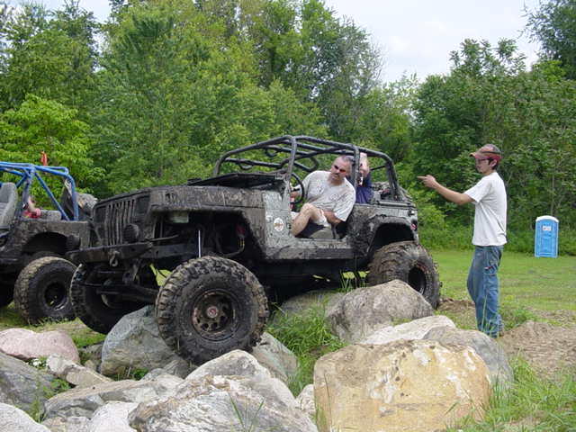 Muddy Jeep Wrangler with roll cage, driver inside, another Jeep to the left