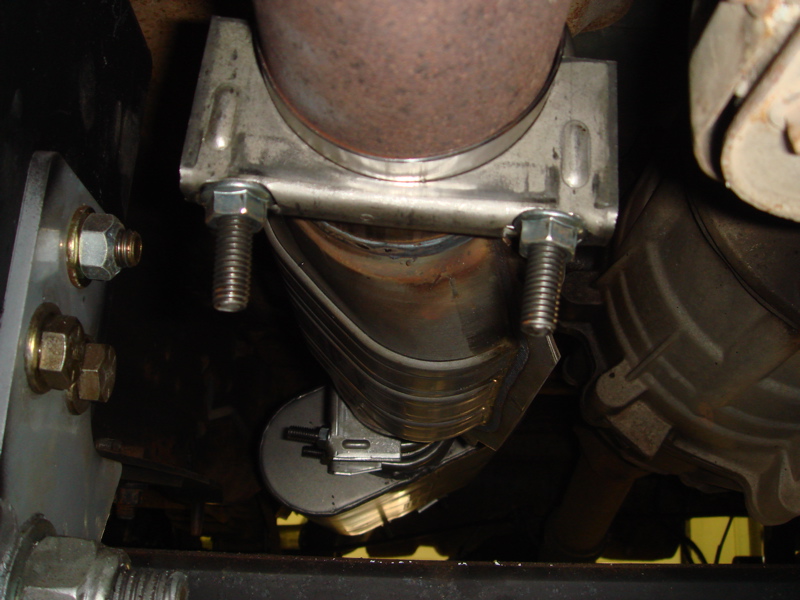 Close-up of a vehicle's exhaust pipe held by a metal clamp with bolts