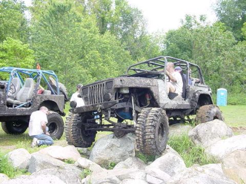 1992 Ford Bronco - Two modified off-road vehicles are positioned on a rocky terrain with trees in the background.
