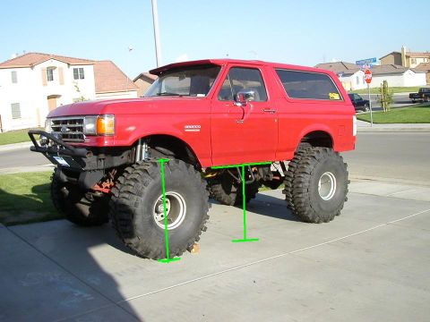 1991 Ford Bronco - This lifted red Ford Bronco is parked on a suburban driveway under a clear blue sky.