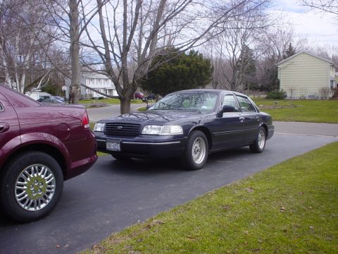 2000 Ford Crown Victoria - A dark blue 2000 Ford Crown Victoria is parked on a driveway next to another vehicle.