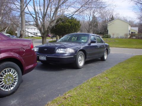 2000 Ford Crown Victoria - A dark blue 2000 Ford Crown Victoria is parked on a driveway next to another vehicle.