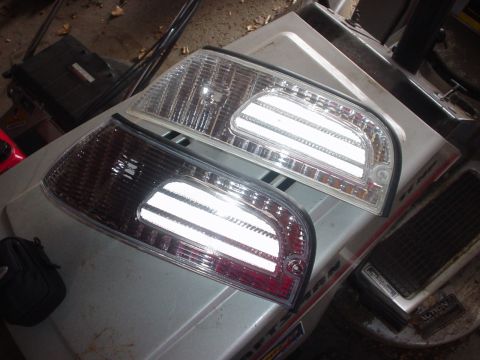 2000 Ford Crown Victoria - A pair of car tail lights, one clear and one smoked, are displayed on a surface.