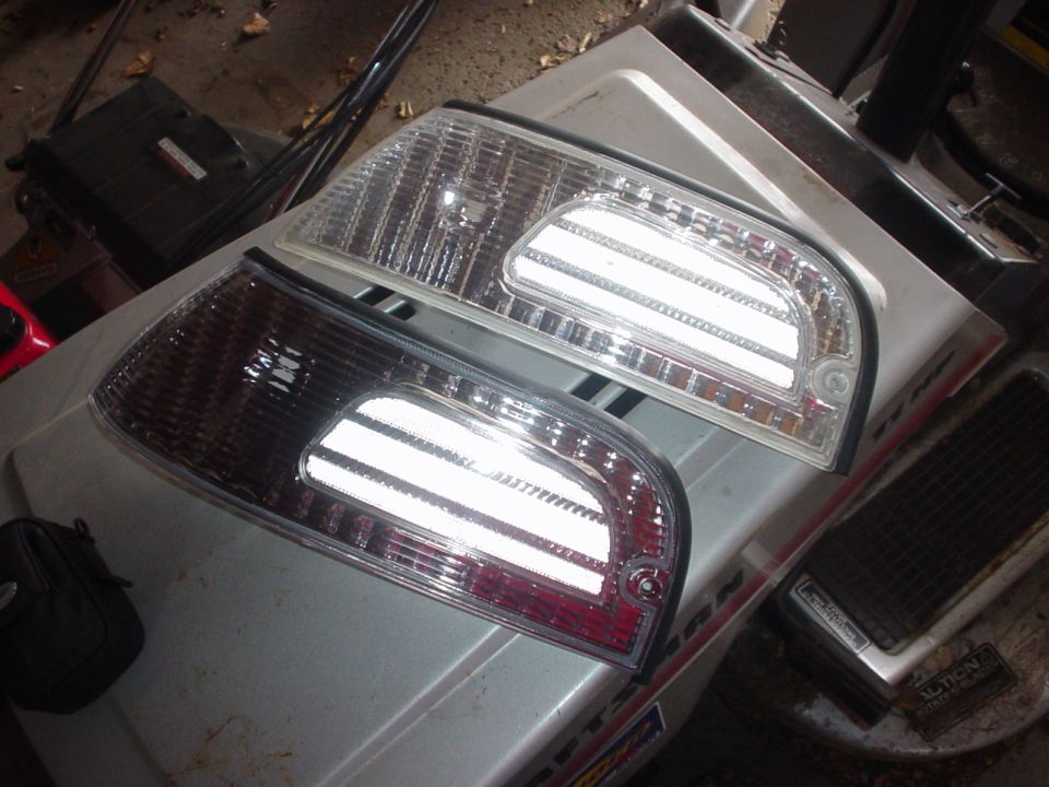 Pair of aftermarket clear tail light lenses with chrome reflectors sitting on a shop machine