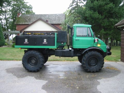 1991 Ford Bronco - A green Unimog truck with large, off-road tires is parked on a paved surface in front of a house.