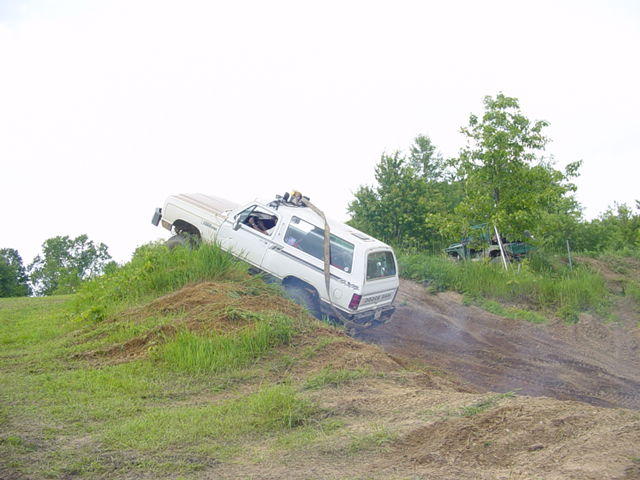 White SUV climbing a steep dirt hill with trees in the background