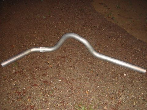 1996 Ford Bronco - Metal exhaust pipe with a label, resting on a dirt and gravel surface.