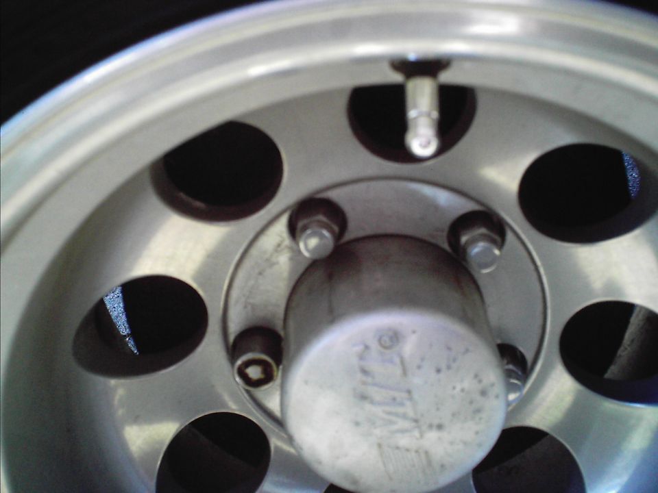 Close-up of a vehicle's aluminum wheel with a silver hubcap that has some text on it