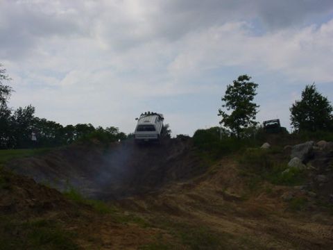 1992 Ford Bronco - A white SUV navigates a challenging off-road course, kicking up dust as it ascends a steep incline.