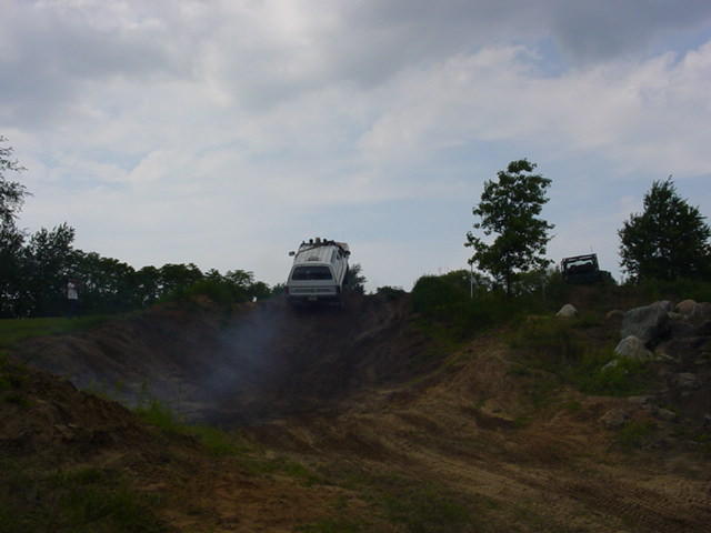 White SUV climbing a steep dirt hill with smoke trailing