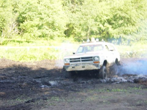 1992 Ford Bronco - A white SUV navigates a muddy track, kicking up dirt and spray.