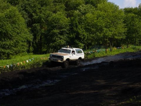 1992 Ford Bronco - White SUV navigates a muddy track with trees lining the path.