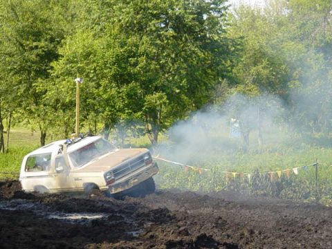 1992 Ford Bronco - SUV is stuck in thick mud, emitting smoke during an off-road event.